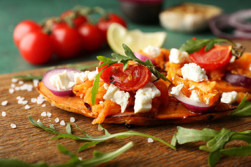 Baked sweet potato with cheese and vegetables on wooden board, closeup