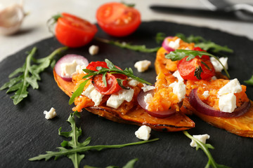 Baked sweet potato with cheese and vegetables on slate plate, closeup
