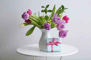 Bouquet of beautiful flowers with gift box on table against light background