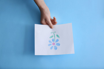 Female hand with picture of beautiful flower on color background