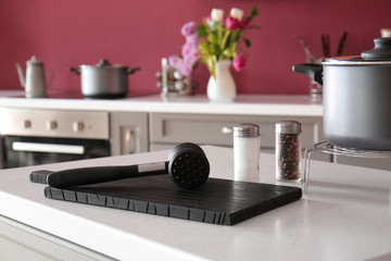 Cutting board with tenderizer and spices on table in kitchen
