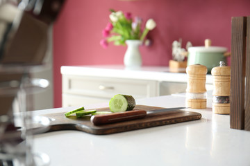 Cutting board with fresh cucumber and knife on table in kitchen