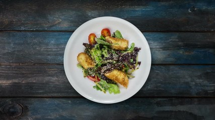 Salad with salmon in breadcrumbs with lettuce and sesame seeds. Rotates on wooden background. Top view