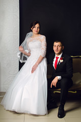 Naklejka premium wedding photoshoot in the Studio. the bride and groom posing. groom with a red tie and black business suit. the bride in a white lush dress