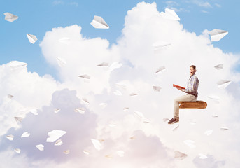 Handsome man student reading book and paper planes flying around