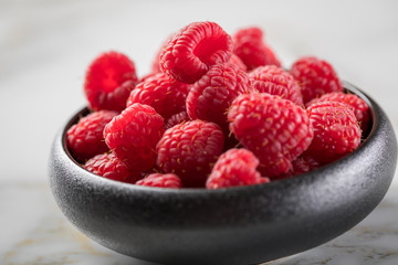 Himbeeren in schwarzer Porzellan Schale auf Marmor Hintergrund