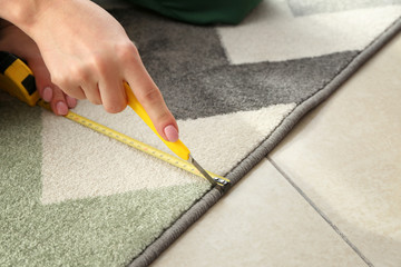 Fototapeta na wymiar Woman with tape measure cutting carpet, closeup