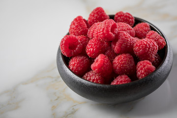 Himbeeren in schwarzer Porzellan Schale auf Marmor Hintergrund