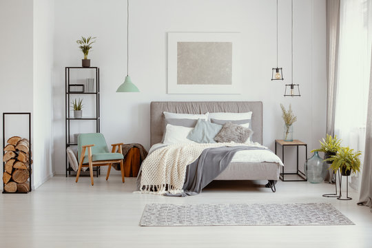 Grey and pastel bedroom design with big comfortable bed with lot of pillows and cozy blankets and abstract silver painting on the wall, real photo