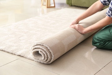 Worker rolling carpet on floor in room