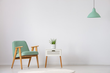 Fototapeta na wymiar Vintage mint armchair next to small white table with green plant in pot in bright interior, real photo with copy space on the empty wall