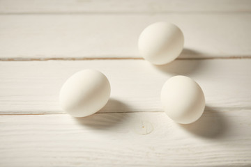 selective focus of uncooked chicken eggs on white wooden planks
