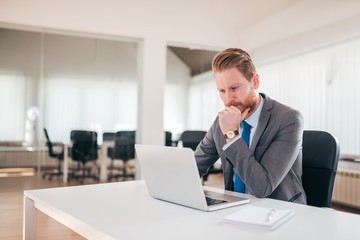 Businessman working on laptop in office, being concerned.