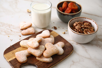 Wooden board with tasty cookies and glass of milk on light table