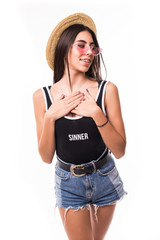 Studio shot of beautiful pleased tourist spends summer holidays abroad, smiles gladfully as has wonderful excursion, wears sunglasses, straw hat, fashionable summer dress, isolated on white wall