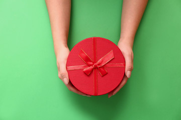 Female hands with gift box on color background