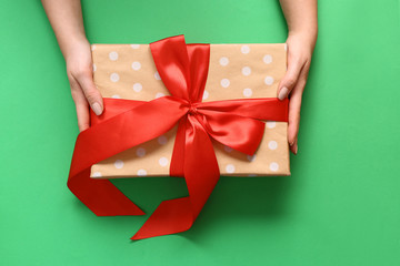 Female hands with gift box on color background