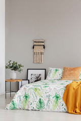 Handmade macrame and copy space on the empty grey wall of elegant bedroom with floral bedding on king size bed