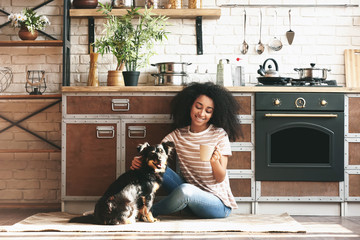 African-American woman with cute funny dog drinking coffee in kitchen