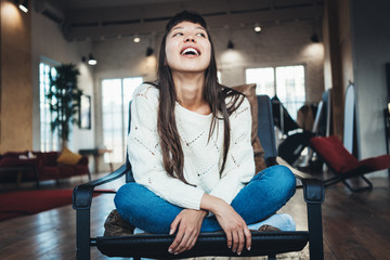 Fototapeta na wymiar Portrait of smiling pretty asian girl sitting in bright spacious room