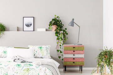 Unique suede covered nightstand with grey lamp in bright scandinavian bedroom with urban jungle, copy space on the empty grey wall