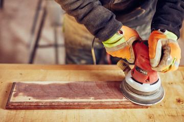 Male carpenter using orbital electric sander in a retro vintage workshop.