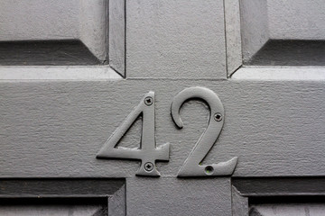 House number 42 with the forty-two painted in grey on a metallic grey door with carved wooden panels