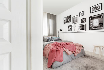 Gallery of posters on white wall in modern bedroom interior with pink sheets on bed. Real photo