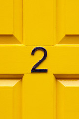 House number two with the 2 in the middle cross bar of a bright yellow painted house door seen...