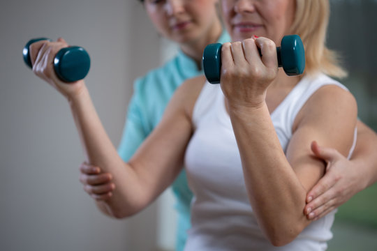 Professional physiotherapist helping senior woman to lift hand weights