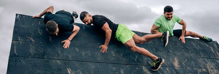 Group of participants in an obstacle course climbing an inverted wall