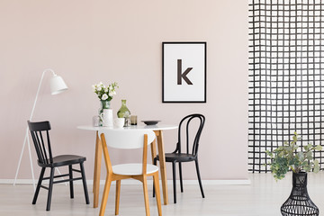 Black chairs at wooden table in modern dining room interior with poster and white lamp. Real photo