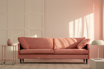Pastel pink couch in white living room interior, copy space on empty wall