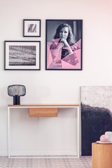 Posters in black frames on white wall in spacious hall with console table with lamp