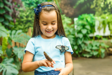 Close up of cute little girl holding butterfly on hand and looking at it