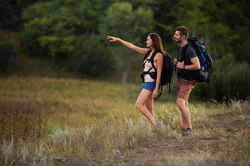 A man and a woman are hiking in the mountains with backpacks. The girl points the right way