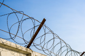Concrete wall with razor barbed tape wire on blue sky background on a Sunny day