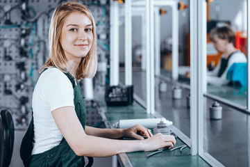 Closeup of concentrated young female worker in denim overall working at factory