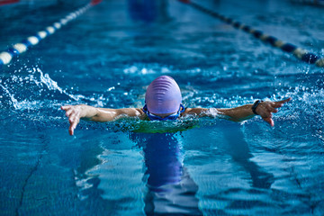 Female athlete swims with a butterfly style. Splashes of water scatter in different directions.