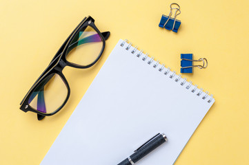 Notebook, eyeglasses and office stationery on bright yellow background