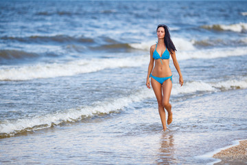 beautiful slender woman in a blue swimsuit walking on the beach