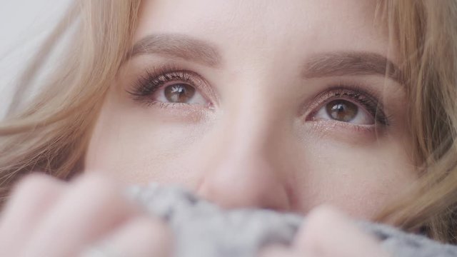 Portrait of a beautiful young girl, wrapped in a cozy fluffy gray plaid. Eyes close-up. The girl has a light Nude makeup and styling curls. Daylight. Slow motion 4K