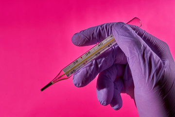 A hand in a medical glove holds a thermometer to measure body temperature