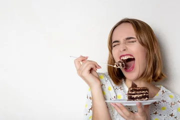 Gordijnen Funny young girl eating tasty chocolate cake over white background. Empty space © vpavlyuk