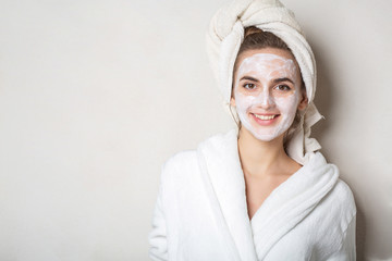 Obraz premium Cheerful brunette model with moisturizing cream mask and bath towel on head. Empty space