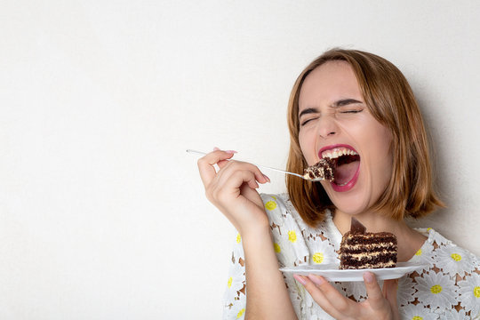 Funny young girl eating tasty chocolate cake over white background. Empty space