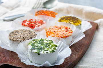 Assortment of French fresh white soft goat cheeses with different tastes topping made with herbs,...