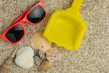 empty yellow plastic toy shovel and red childrens sunglasses on the beach with seashells