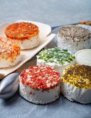 Assortment of French fresh white soft goat cheeses with different tastes topping made with herbs, paprika, indian curry, bruscetta, chives and dried tomatoes
