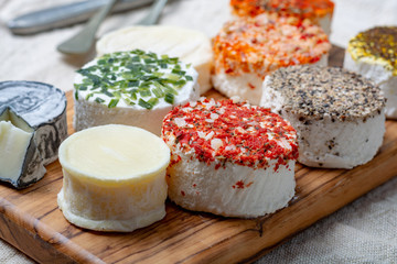 Assortment of French fresh white soft goat cheeses with different tastes topping made with herbs, paprika, indian curry, bruscetta, chives and dried tomatoes
